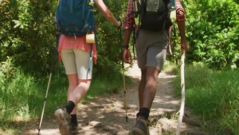 Happy-diverse-couple-hiking-with-backpacks-in-park,-slow-motion