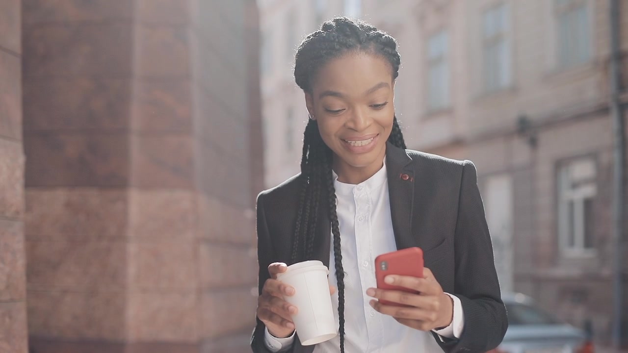 Giovane Donna d'Affari che Usa lo Smartphone e Tiene una Tazza di Caffè all'Aperto
