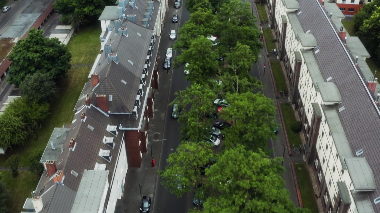 Un'auto percorre una strada alberata di Colonia mentre un drone si inclina verso l'alto per rivelare la città.