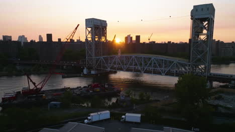 Drone-shot-of-a-train-crossing-the-Park-Avenue-Bridge,-sunny-evening-in-Harlem,-NY