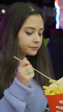 young woman eating french fries with a stick