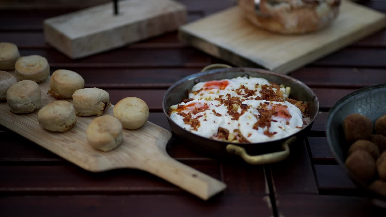 wooden table set with cheese rolls fried balls and a skillet of creamy egg and chips