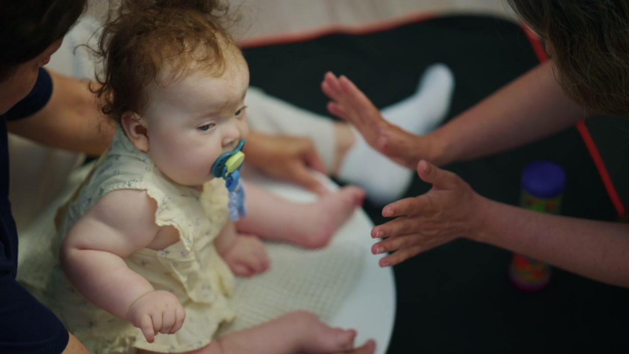 Close up overhead footage of a baby's legs and feet resting on an adult's lap during a calm indoor therapy or caregiving moment