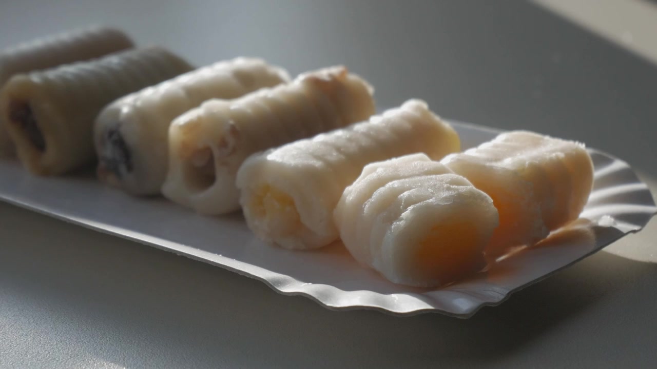 Kue Marzipan Tradisional Spanyol "Huesos de Santo" di Atas Piring Kertas, dengan Sorotan Cahaya Lembut.