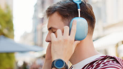 happy handsome man in wireless headphones choosing listening music dancing outdoors city street
