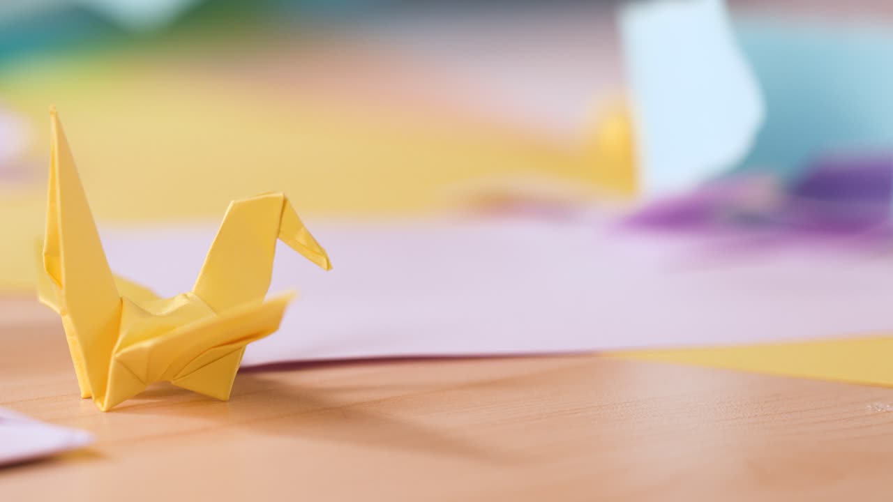 A close-up shot of a yellow paper crane on a desk with soft natural lighting