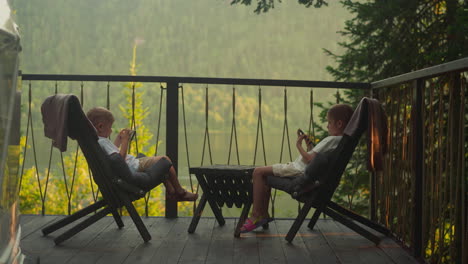 little girl and boy sit together in furry armchairs on outdoor terrace. children rest enjoying calm nature scene. fantastic scene of untouched woodland