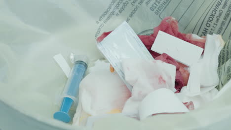 bloodied sponges syringe in waste bag in surgery. blood-covered sponges and discarded syringe lie in bag during coronary artery bypass procedure in hospital