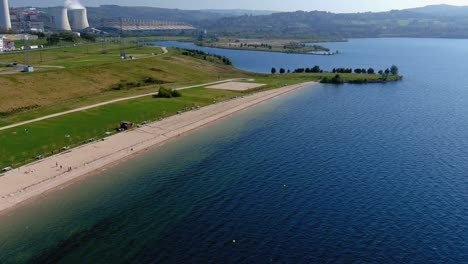 gente disfrutando de la planta de energía térmica de la playa del lago con jardines y agua limpia en una tarde soleada