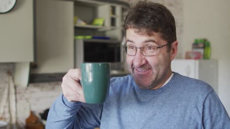 smiling and relaxed caucasian man drinking coffee in kitchen at home