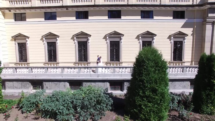 Coppia Di Sposi Vicino All'Antico Edificio. Ripresa aerea di una coppia di sposi che ride, tenendosi per mano mentre cammina su un balcone.