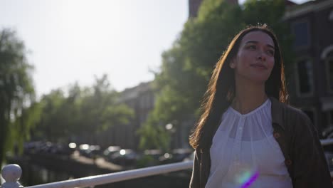 Model-woman-walks-along-bridge-over-river-in-historic-urban-city-district