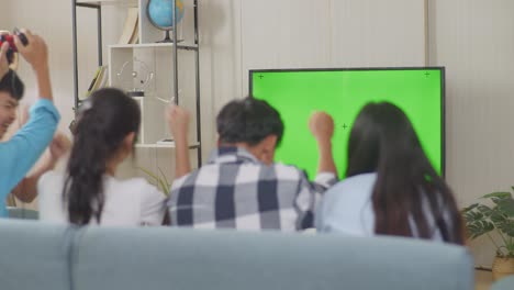 asian teenagers playing video games with tv green screen and celebrating victory at home, mock up tv green screen