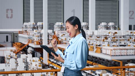 side view of happy asian business woman celebrating using tablet in the warehouse