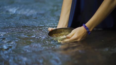 A-woman-collects-water-with-a-vessel-in-the-river-in-the-Salto-Encantado-park-located-in-Misiones,-Argentina