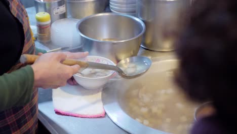 slow motion shot of woman pouring soup in bowl at street market in taiwan