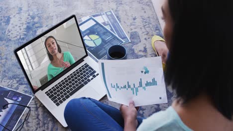 african american woman holding a document having a video call with female colleague on laptop