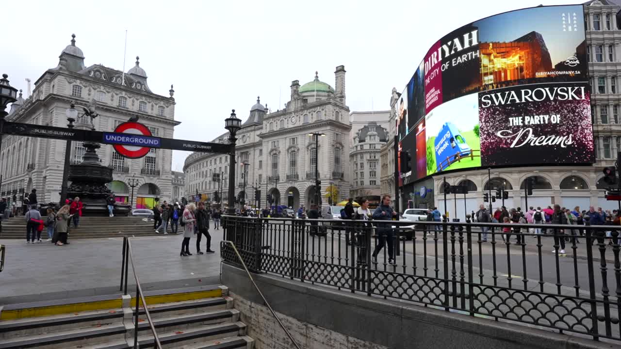 Piccadilly Circus in London with iconic LED screens and a few people by the underground entrance