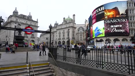 piccadilly circus in london with iconic led screens and a few people by the underground entrance