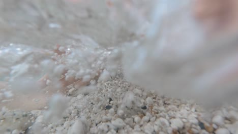 slow motion underwater: child's hands playing over white pebbles in crystal clear sea