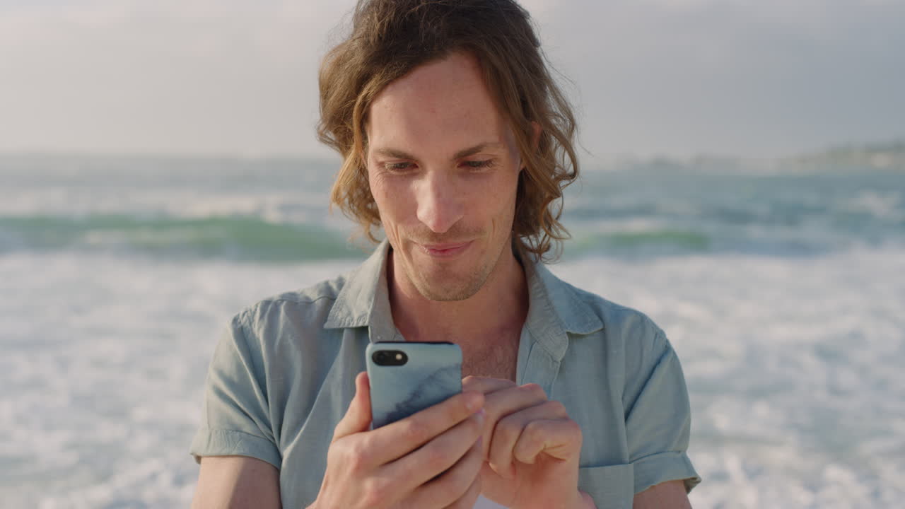 portrait of happy young man using smartphone texting browsing online sharing vacation experience on social media enjoying mobile communication in sunny beach background
