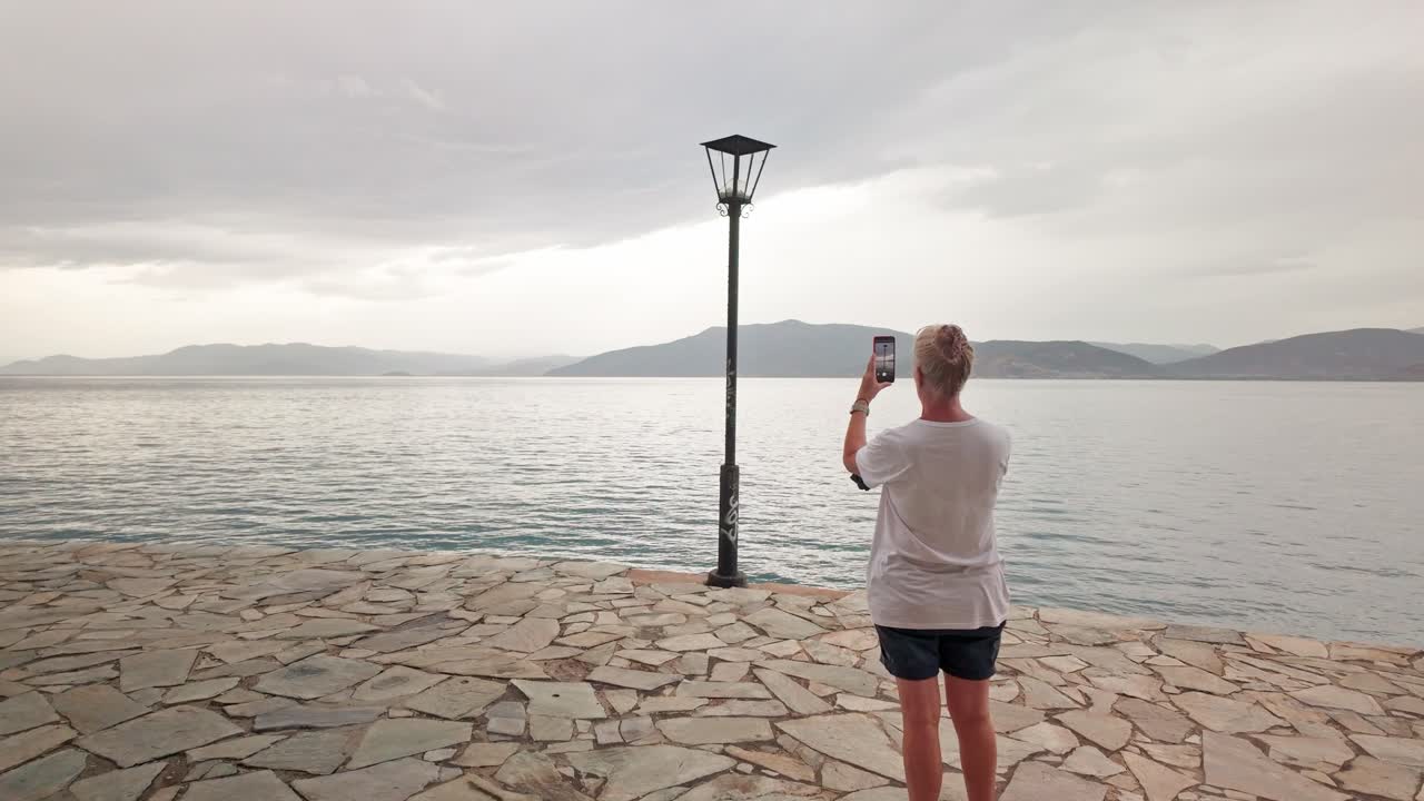 Woman photos Lampost on Greek coastal path distant Mountain horizon