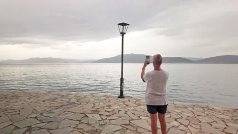 woman photos lampost on greek coastal path distant mountain horizon