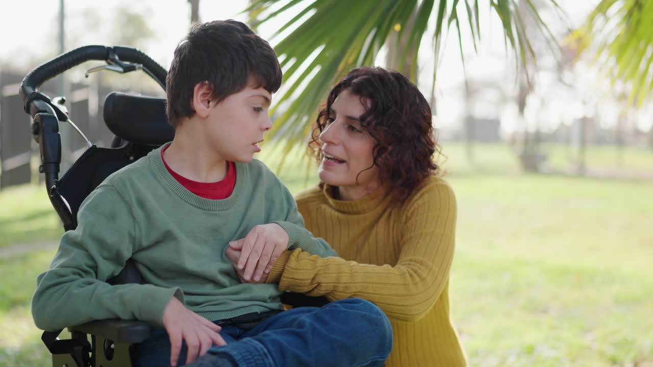 A woman supports a child in a wheelchair outdoors