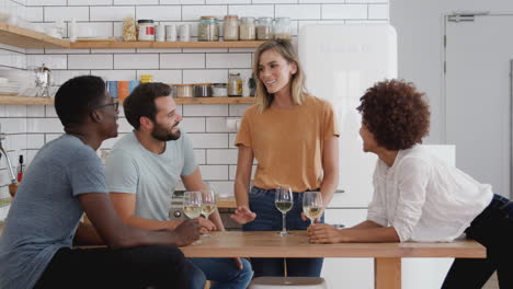 two couples relaxing in kitchen around kitchen counter at home and drinking wine together