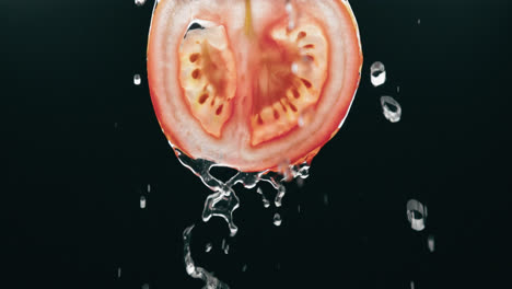 agua que fluye por rodaja de tomate fresco en cámara lenta con fondo negro retroiluminado