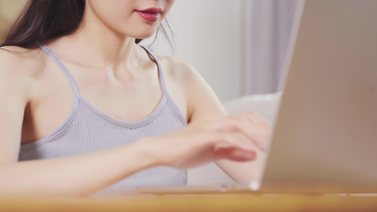 女员工坐在沙发上，使用笔记本电脑和平板电脑工作，同时使用便携式手持迷你风扇。在家中，感到压力和烦躁的女孩呼吸着凉爽的新鲜空气，应对夏季炎热天气，进行降温和自我护理。