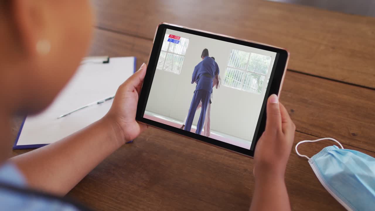 태블릿에서 유도 경기를 보는 얼굴 마스크로 테이블에 앉아 있는 여성의 합성