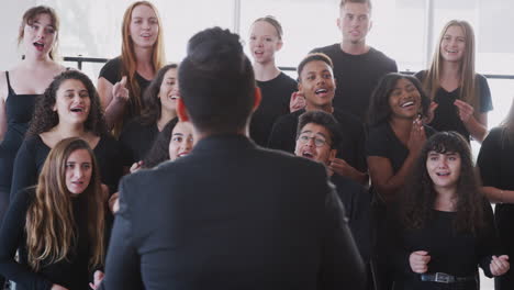 male and female students singing in choir with teacher at performing arts school