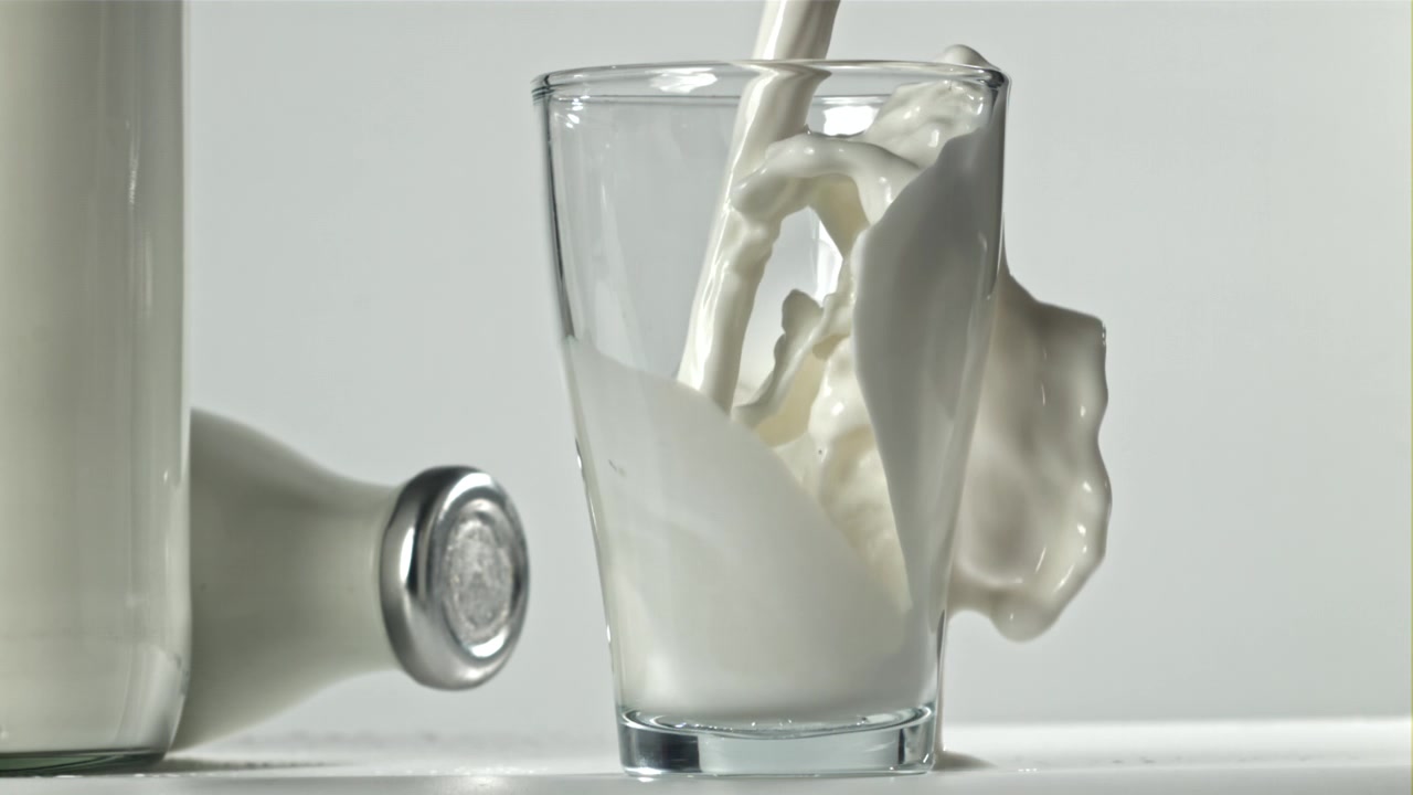 Latte che si versa in un bicchiere e trabocca al rallentatore