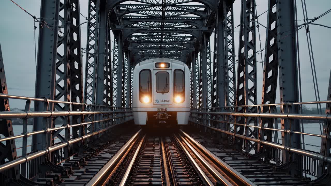 Un treno si avvicina su un ponte d'acciaio, ripreso da una prospettiva dal basso, creando un effetto drammatico
