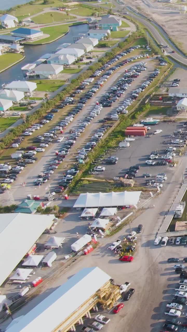 Vertical drone shot capturing the busy Grand Isle Marina, hotel, and Tarpon Rodeo Pavilion surrounded by full parking lots and festival activity during the Island Strong Music Festival