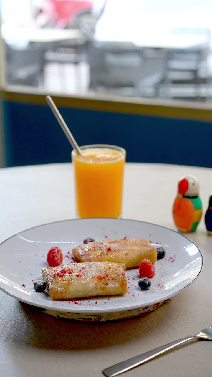 Fluffy homemade pancakes stacked on white ceramic plate, garnished with fresh blueberries and raspberries, dusted with powdered sugar, served alongside vibrant orange juice