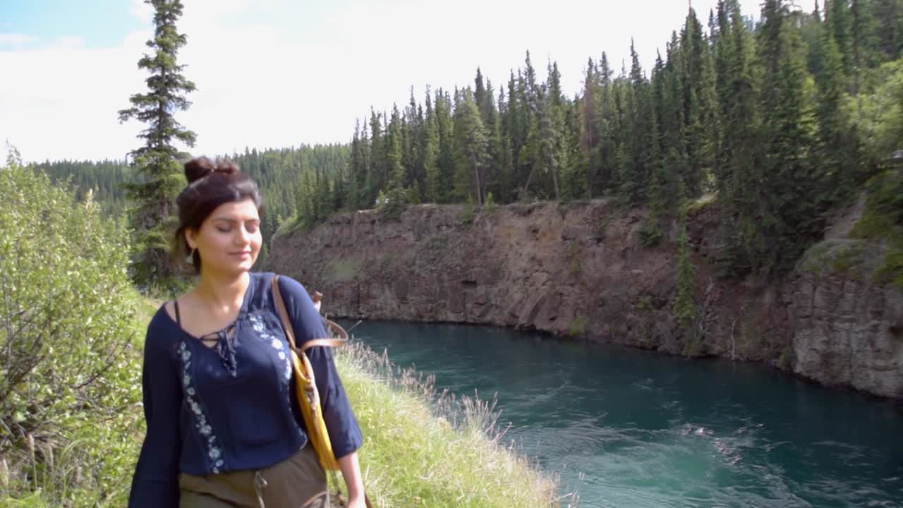 Mujer indígena camina junto al río Yukón, plano medio.