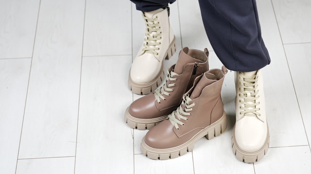 Model puts on the floor a similar beige pair of boots to those she's wearing. Female demonstrating stylish modern footwear. Top view.