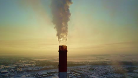 industrial smoke stack at sunrise/sunset over a snowy cityscape