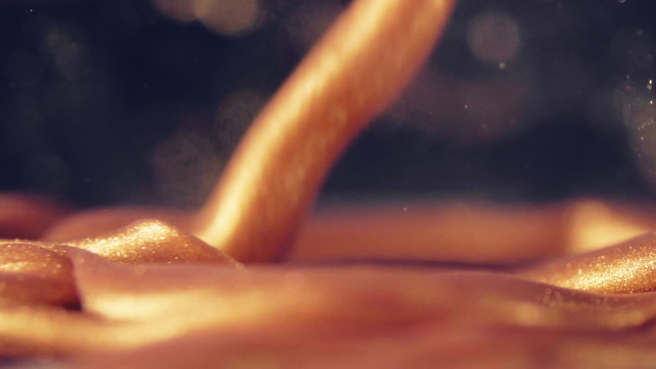 황금 잉크 입자는 검은 바탕에 다채로운 혼란으로 물에 흐른다.