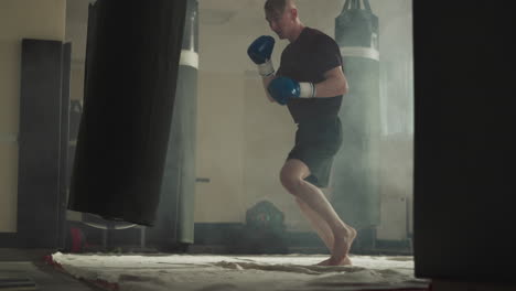 kick-boxer patea saltando bolsa de boxeo en el gimnasio. atleta hábil muestra diferentes técnicas de lucha en el gimnasio a cámara lenta. entrenamiento de combate activo en el humo