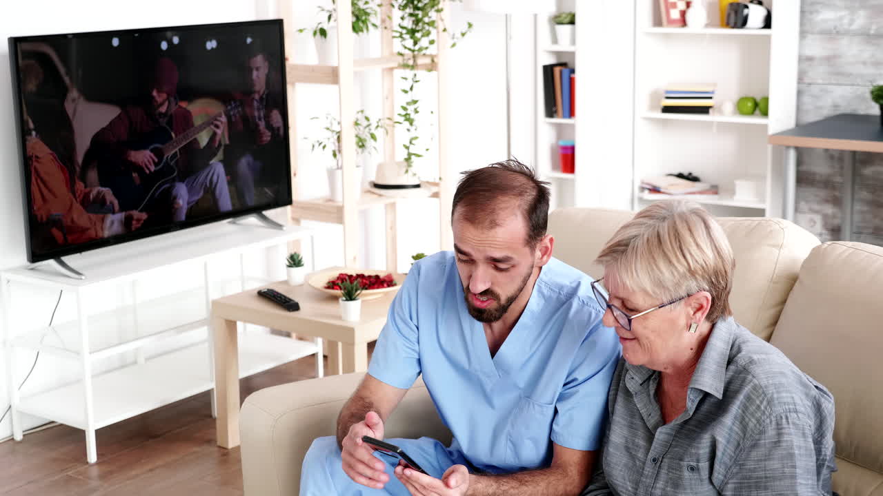 enfermera masculina en una casa de retiro ayudando a una anciana a usar su teléfono