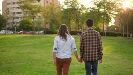 couple holding hands and walking through a park at sunset