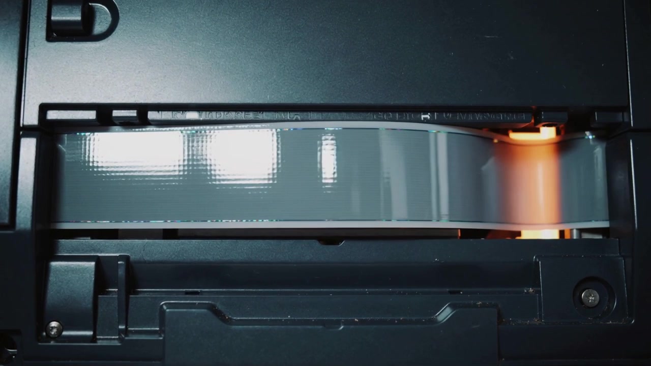 Advancing thin belt bulging right across device slot, driven by roller revealing orange light