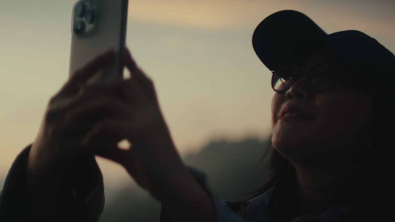 Woman taking photos of a beautiful sunset over a lake from a mountaintop