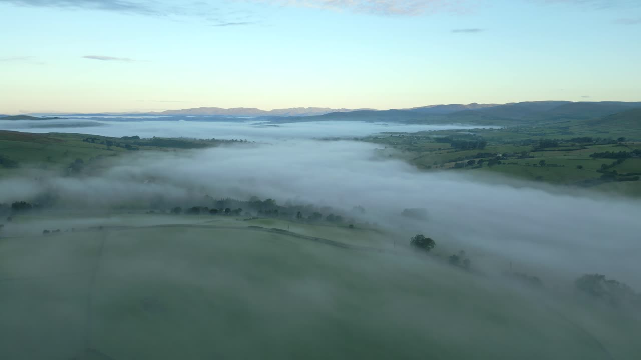 volando alto sobre los campos verdes y brumosos hacia la niebla en el valle al amanecer