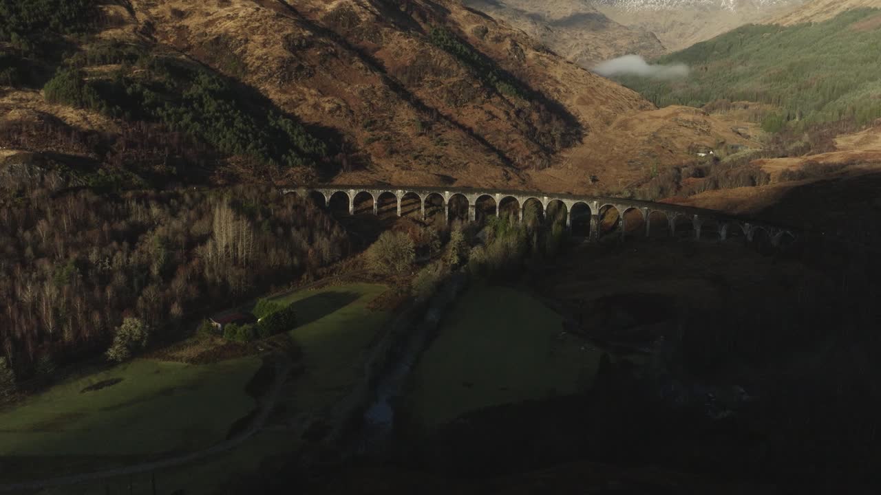 Scenic view of a stone viaduct spanning a valley with river, hills, and green fields on Isle of Skye