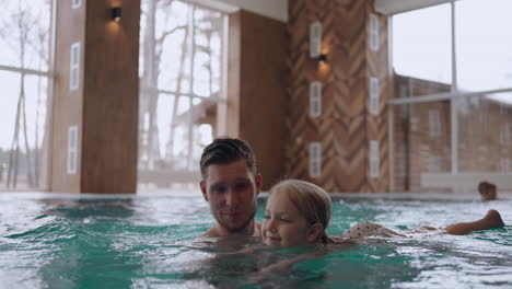 happy childhood and parenthood father is teaching is little daughter to swim in swimming pool