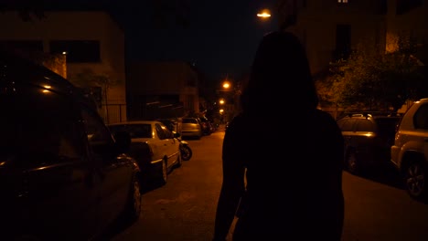 Night-shot-of-a-woman-walking-down-a-road-with-parked-cars-on-both-sides